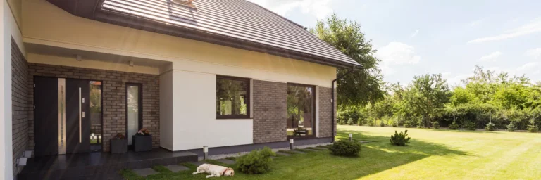 Residential home with dog laying on green lawn.